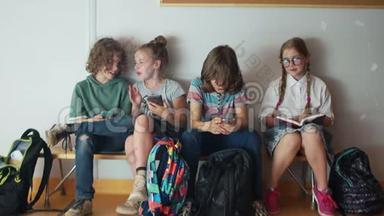 三个青少年对他们的手机充满热情。 最好的学生坐在他们旁边读一本书。 小学生和小学生